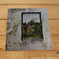 Front cover of Led Zeppelin IV album showing iconic elderly man with bundle of sticks against peeling wallpaper background