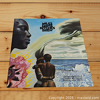 Front cover of Miles Davis Bitches Brew double LP showing colorful illustrated design with ocean and figures.
