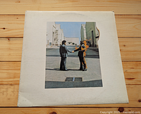 Front cover of Pink Floyd "Wish You Were Here" vinyl LP album, showing two men shaking hands, one man on fire in an industrial setting.