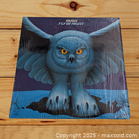 Front cover of Rush Fly By Night vinyl LP record showing blue owl artwork sealed in shrink wrap on wooden background.