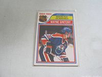 Front side of Wayne Gretzky 1984-85 OPC Assist Leader hockey card showing image of Gretzky skating in Oilers uniform with title and league logo