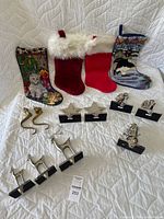 Four fabric Christmas stockings and ten metal stocking hangers displayed on white quilted surface.