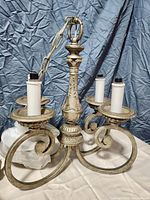 Metal chandelier with four arms, decorative central column, and sockets for bulbs. Shows extra chain and switch included.