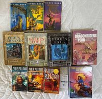 Photo of 11 books arranged on a fabric surface showing titles and cover art of visible wear fantasy book series and compendiums.