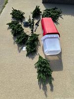Overview of artificial Christmas tree branches, trunk sections, and storage bin with lid arranged on ground.