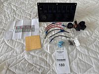 Full lot overview showing 8-gang switch panel, wiring, connectors, label stickers, instruction sheet, and accessory components laid out on a white quilted surface.