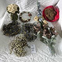 Top-down photo showing white rose bouquet, wreath, multiple berry garlands, artificial foliage stems, and bag of moss all arranged on a white quilted fabric.