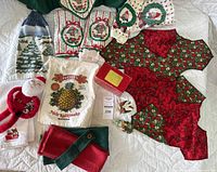 Wide shot of assorted Christmas and holiday kitchen linens and decor including potholders, towels, placemats, and plush items laid on white quilted surface