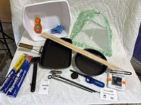 Full view of camping gear set including LuminAID lantern, skewers, lighter, pans, tongs, white plastic tub, and green mesh cover.