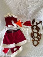 Red and white Santa hats, red shorts, Santa beard with hat, reindeer antler headbands, and elf hat on white quilted background.