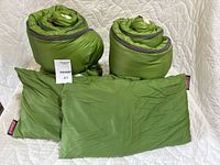 Photo showing two rolled green sleeping bags and two matching green pillows on a quilted surface.