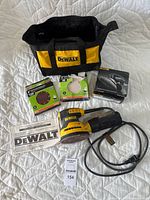 Overview of lot with DeWalt DWE6421 sander, DeWalt soft bag, sanding discs packages, and manual displayed on bed.