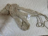 Coiled off-white rope hammock with attached hanging loops shown on a quilted fabric surface.