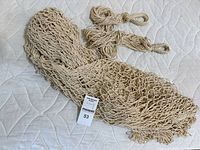 Folded beige net-style hammock laid out on a white mattress surface, showing the netting and hanging loops.