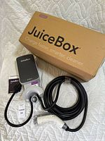 Charging station with coiled charging cable, NEMA 14-50 plug, user documentation, and original box laid out on a quilted bedspread.