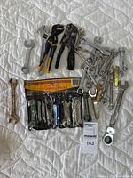 Close-up photo of the hand tools laid out on a white quilted surface showing various wrenches, pliers, and a wrench set in packaging