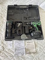 Hitachi cordless drill kit with drill, flashlight, batteries, chargers, drill bits, manuals, warranty, all arranged inside molded plastic carrying case.
