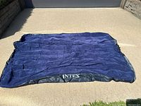 Full view of the navy blue Intex inflatable bed laid flat on a concrete surface, showing its size and surface texture.