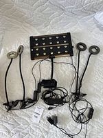 Full lot laid out on white quilted background showing black LED grow light panel with multiple LEDs, two dual-arm ring lights with clamps and cords tangled in the center.