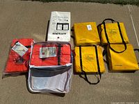 All nine flotation devices, life jackets, and rescue gear laid out on the ground with visible storage bags and instruction labels.