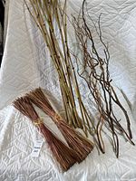Photo displaying all four bundles: two reed bundles, one bamboo bundle, and one curly willow bundle, arranged on a white quilted surface.