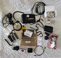 Photo of all items including air compressor, flashlights, phone lenses, magnetic sheets, audio converter, cables, pins and Bob's Big Boy figure arranged on quilted white blanket.