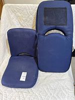 Two blue West Marine Go-Anywhere Seat 2 portable boat seats placed upright on a white quilted surface. One seat shows visible wear with some stains and a tear near the zipper handle.