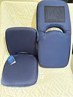 Pair of blue portable boat seats with backrest handles, one showing mesh pocket on back. Clean upholstery shown against light quilted fabric background.