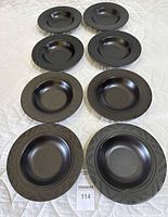 Front view of 8 black stoneware soup bowls arranged in two columns of four, showing the glossy finish and embossed rim detail.