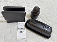 Set of four matte black ceramic kitchenware pieces: napkin holder, butter dish with lid, salt shaker arranged on a cloth backdrop.