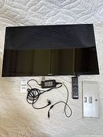 Front view of Samsung 32-inch television with remote, power adapter, and wall mount laid out on quilted surface.