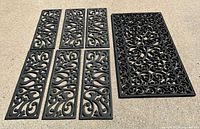 Photo showing 6 smaller narrow decorative black rubber stair treads and 1 larger decorative door mat with scrollwork.