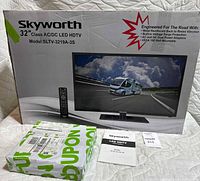Photo of the boxed Skyworth 32 inch LED HDTV showing front of box with image of TV and included remote, with nearby smaller box and manual documents.