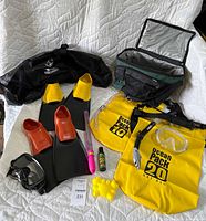 Wide shot of all snorkeling and beach gear items laid on white bedspread showing fins, masks, bags, cooler, and accessories