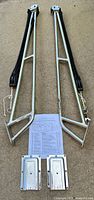 Two davit arms with lines, pulleys, hooks, cleats, two mounting plates, and instruction sheet laid out on concrete