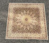 Photo of the rug laid out flat on a surface showing beige and sage colored intricate medallion design.