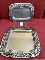 Two rectangular serving trays with black Reggae pattern border on silver metal, placed on red fabric surface. One tray is larger, the other smaller.