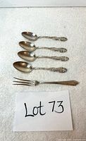 Set of four sterling silver small spoons and one sterling silver small seafood fork arranged on a white cloth.