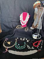 Full view of assorted costume jewelry on black cloth, includes necklaces and bracelets of various materials and colors