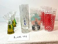 Photo showing all glasses in the lot arranged on a white surface, includes carnival cocktail glasses, tall monogrammed Courvoisier glasses, Dominion tri-coloured glasses, and Libbey ivy design glasses.