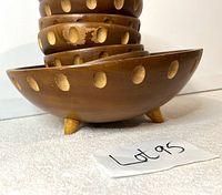 Side angle of the large footed teak bowl showing three short legs and round cut-outs on the exterior. Visible surface wear and scratches noted.