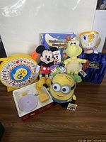 Overview photo showing lot contents of Disney and Nintendo plush toys, vintage See and Say, photo album, Fisher Price record player, and Disney book