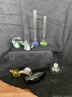 Two tall bubble glass vases, two clear green-and-white swan glass figurines, black and amber glass bird figure, Avon yellow rose and green duck collectibles.