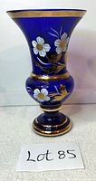 Front view of cobalt blue glass vase with white flowers and gold trim on pedestal base