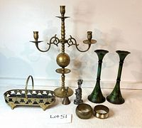 Full view of all items included in the lot showing brass candelabra, candlesticks, filigree basket, llama bell, bracelets, appetizer picks, and small figurine.