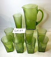 Full set of one vintage avocado green glass pitcher and nine matching glasses arranged on a white background, showing spiral optical swirl patterns.