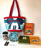 Full view of lot items including Mickey Mouse tote bag, tumbler, decorative plate, three vintage Disney books, and Mickey Mouse pin on a white surface with lot number.