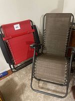 Two reclining outdoor lounge chairs, one red and one brown, shown indoors against a wall.