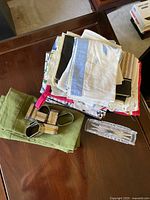 Image showing a stack of assorted folded table linens in different colors and patterns along with clear glass and metal-tone geometric napkin rings on a dark wooden surface.