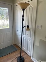 Full view of a bronze metal floor lamp with a large cream glass bowl shade on top and smaller cream glass reading light attached to the pole at mid-height. Positioned near a door and white closet doors.